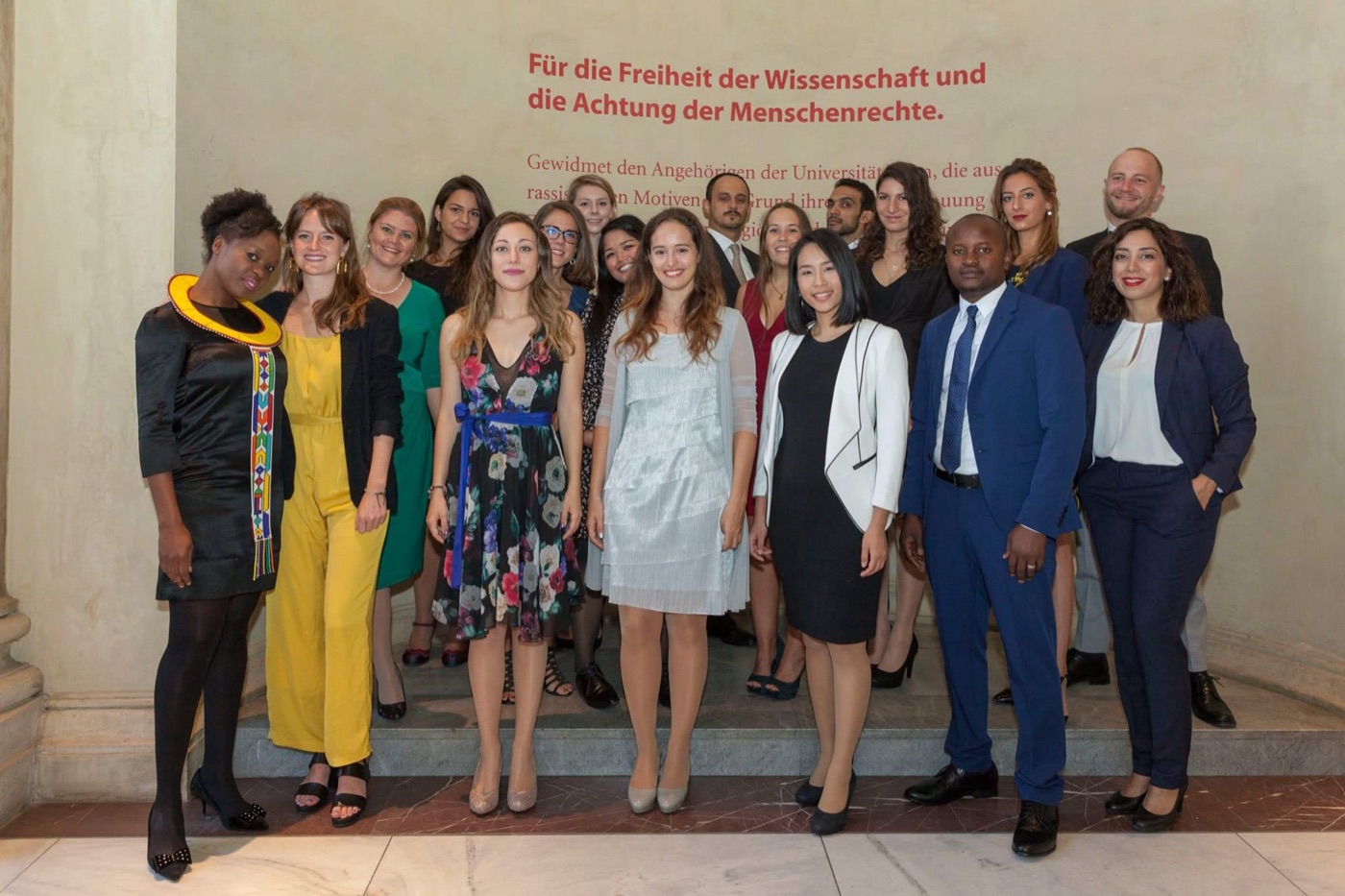 Graduating class of the Master of Human Rights in front of the University of Vienna wall reading Für die Freiheit der Wissenschaft und die Achtung der Menschenrechte